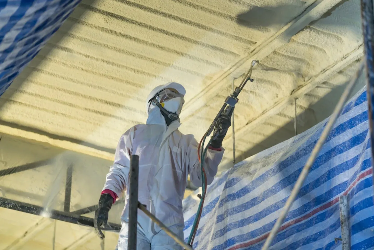 Installer spraying foam overhead with protective sheeting in place